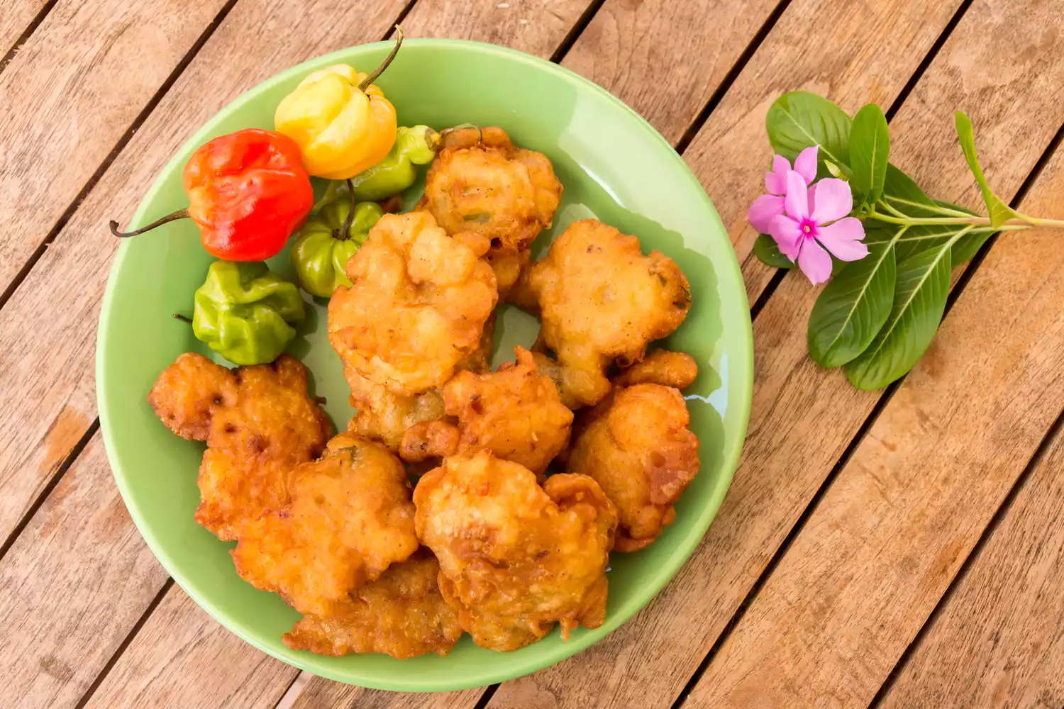 A plate of golden-brown salt cod fritters served with hot peppers.