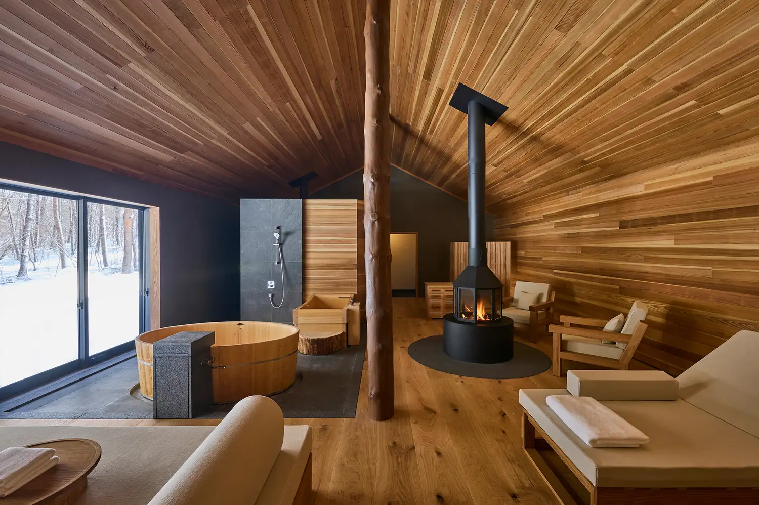 A modern wooden sauna room with a view of the snowy woods through large windows.