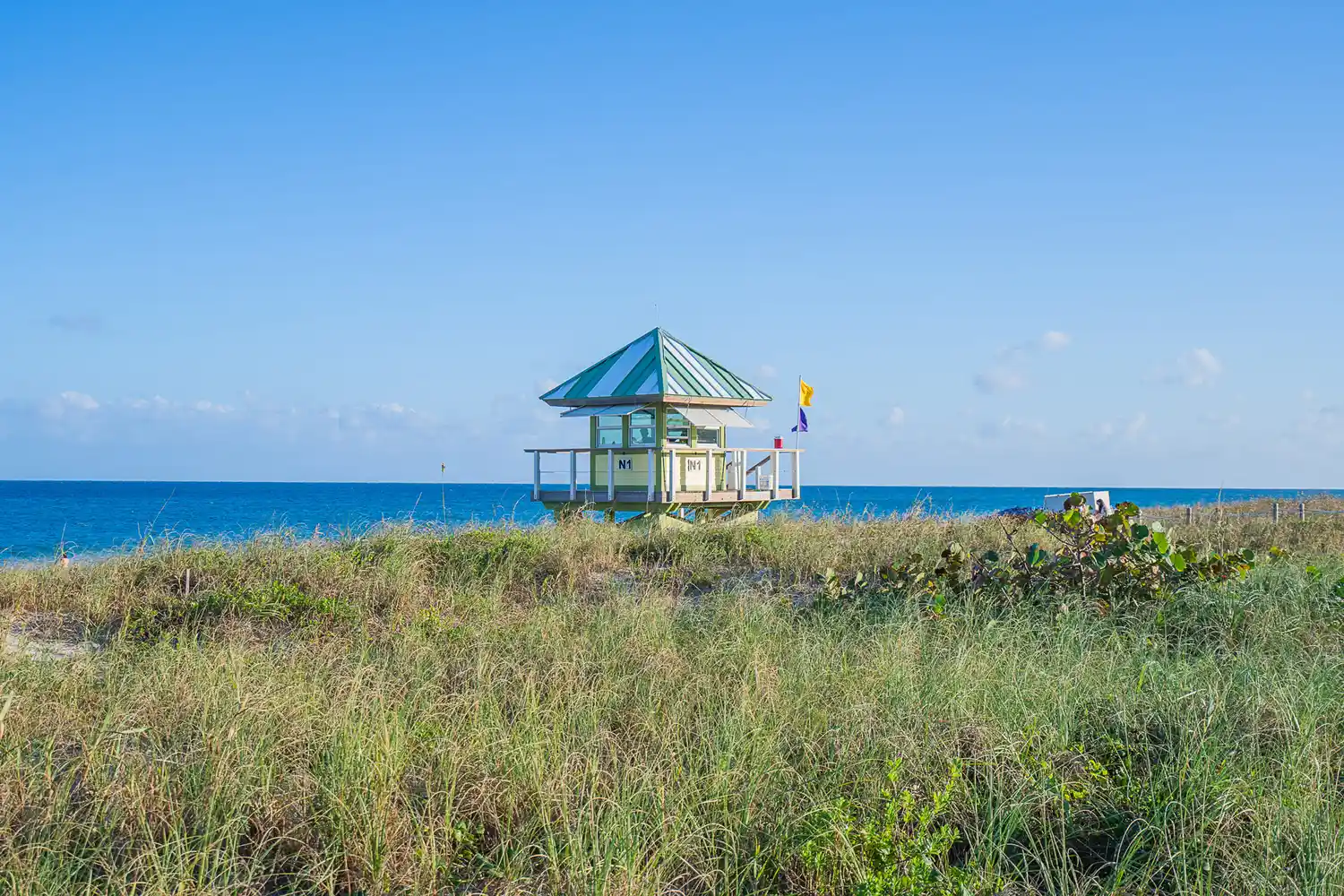 A bright yellow and blue lifeguard stand overlooking the grassy dunes and ocean at Delray Beach.