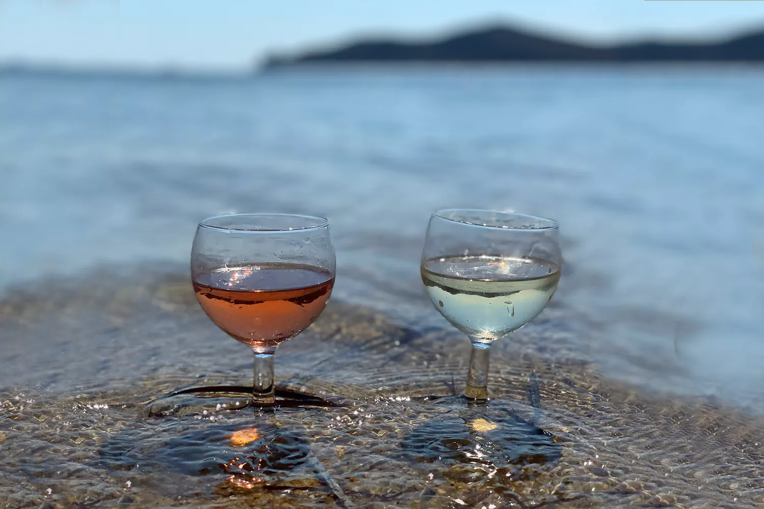 Two glasses of white wine held over the clear blue waters of the Aegean sea.