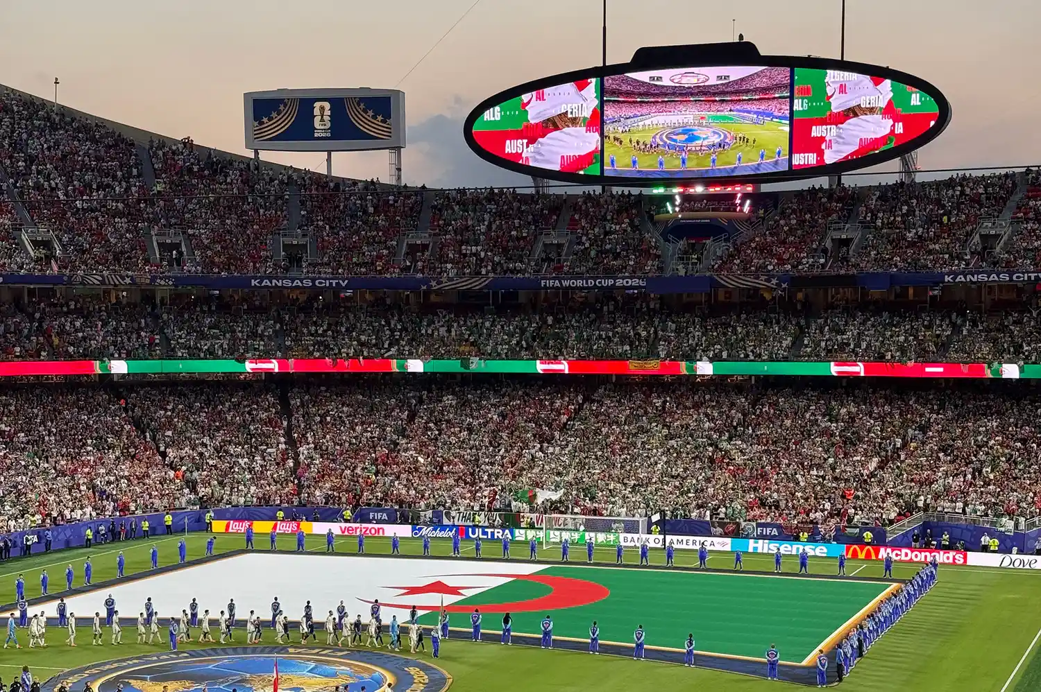 A wide shot of a full stadium with a large Algerian flag displayed on the field during a 2026 World Cup opening ceremony.