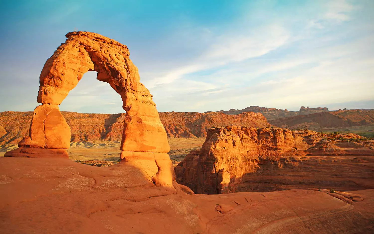 The iconic red sandstone Delicate Arch standing against a desert mountain background.