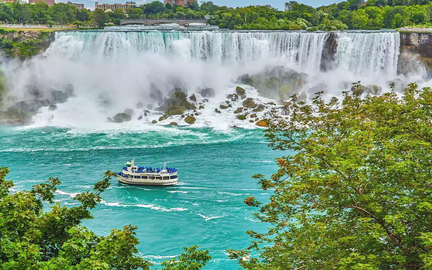 A tourist boat navigating the misty waters at the base of the massive Niagara Falls.