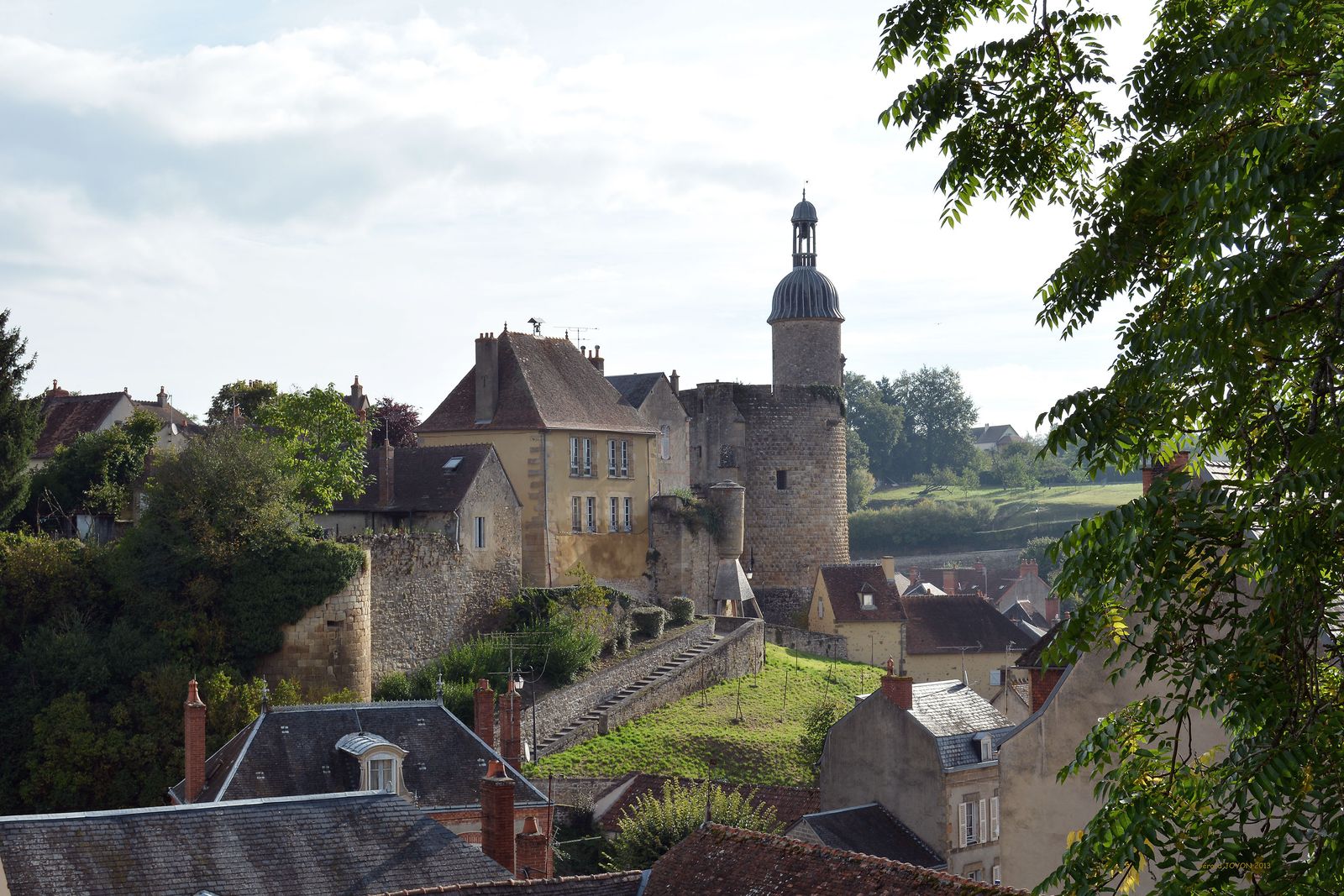 A medieval stone castle and monastery complex perched on a hill in rural France.