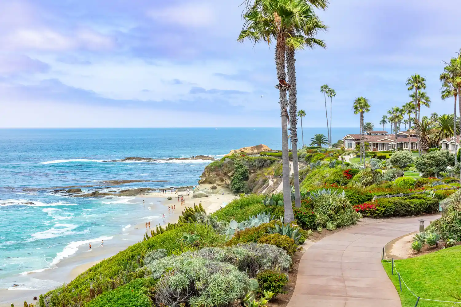 A paved coastal walkway in Laguna Beach California with palm trees and ocean views.