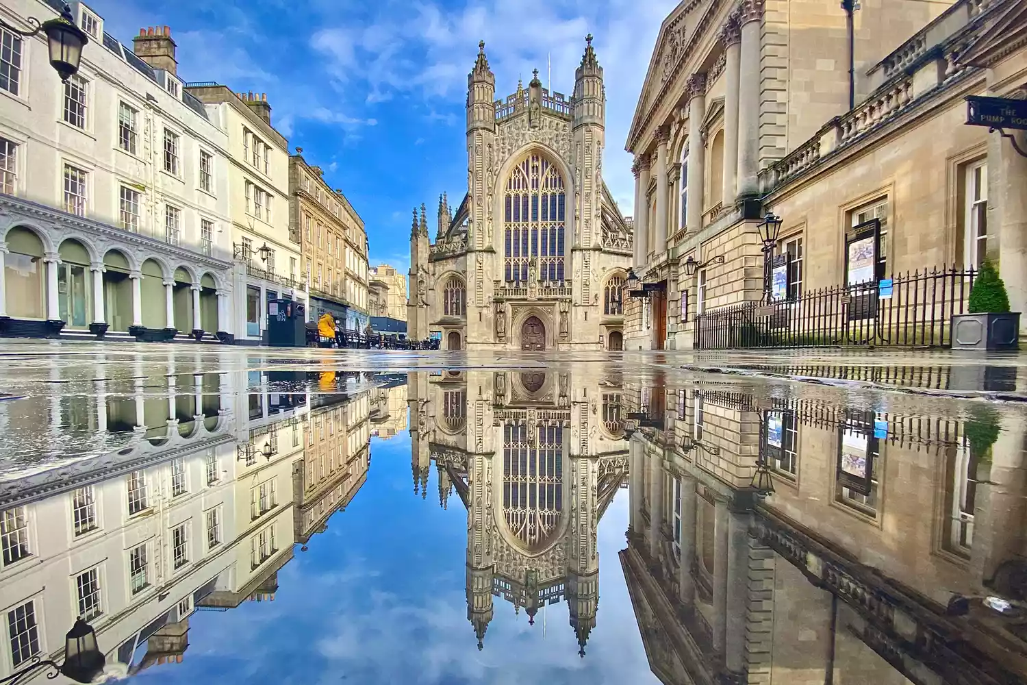 The historic Bath Abbey and Roman Baths reflected in a still pool of water in Bath, England.