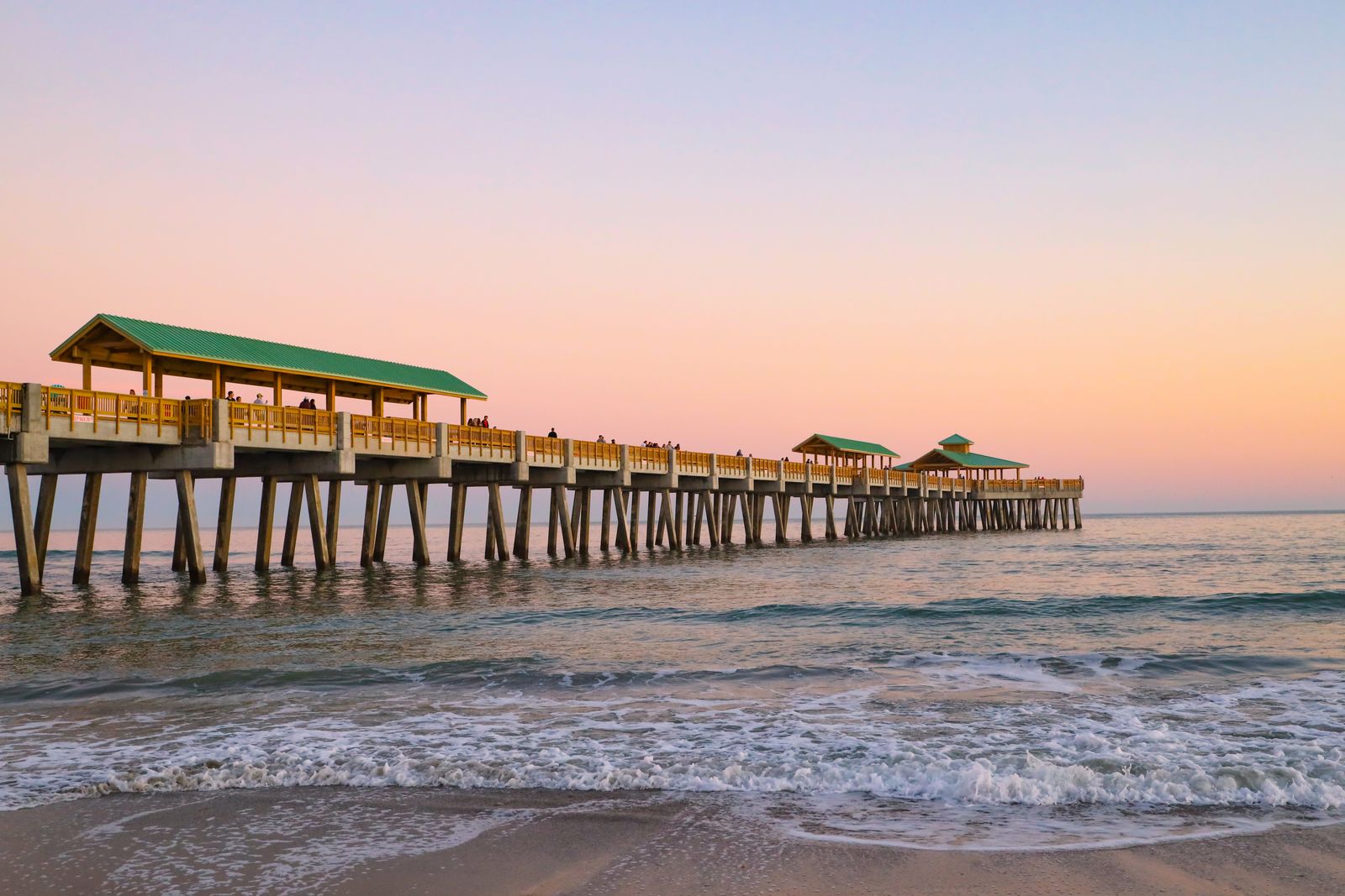 A long wooden pier stretching out over the ocean water under a clear horizon.