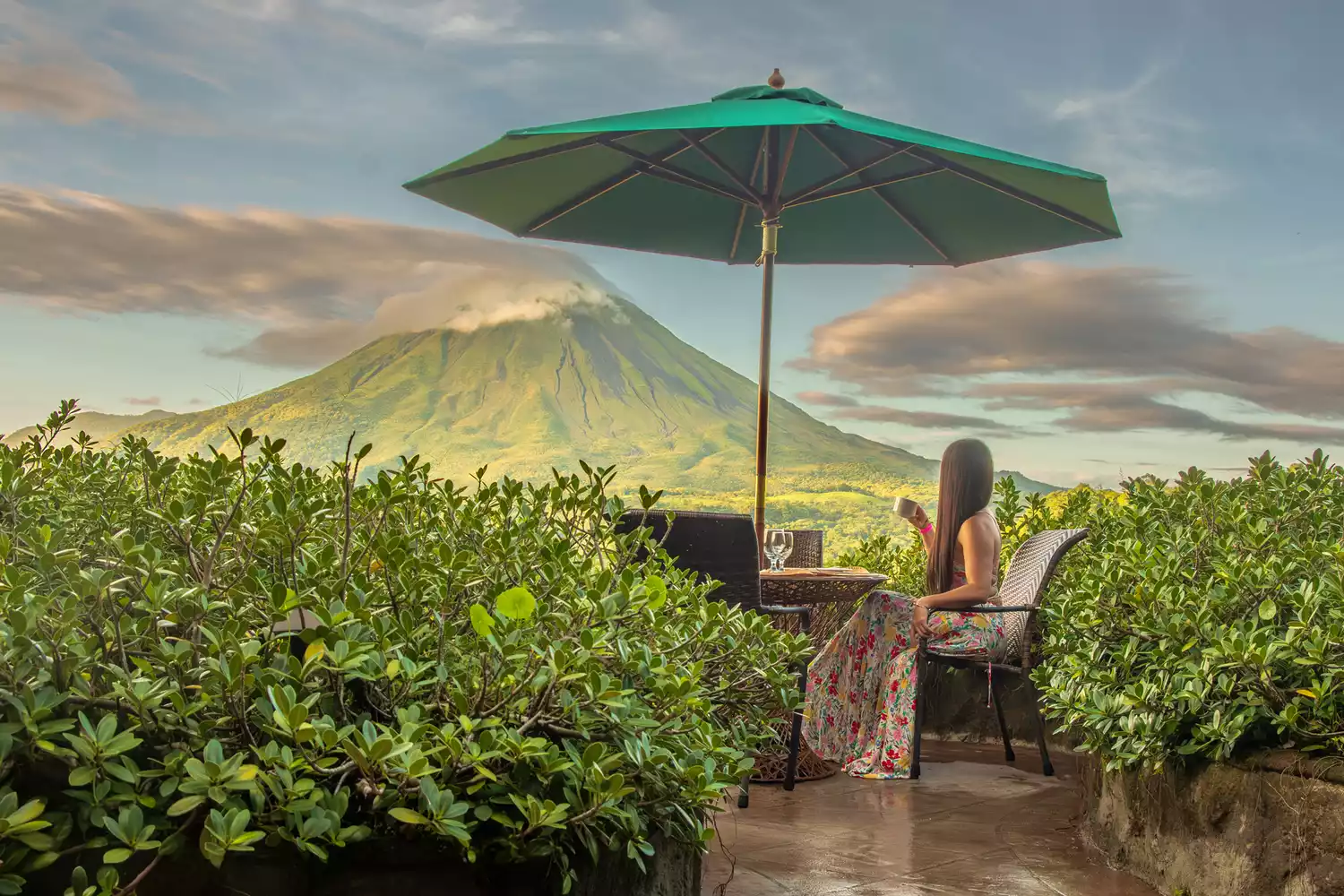 A woman drinking coffee on a terrace with the Arenal Volcano visible in the distance in Costa Rica.