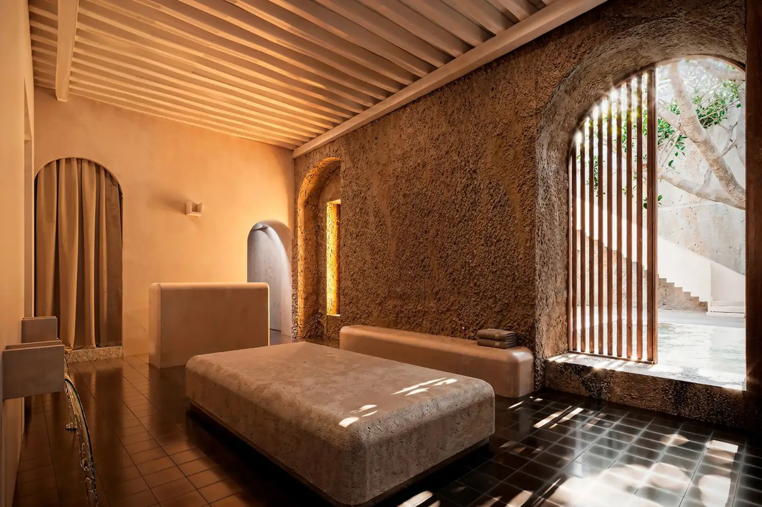 A spa interior with textured stone walls and natural light filtered through wooden slats.