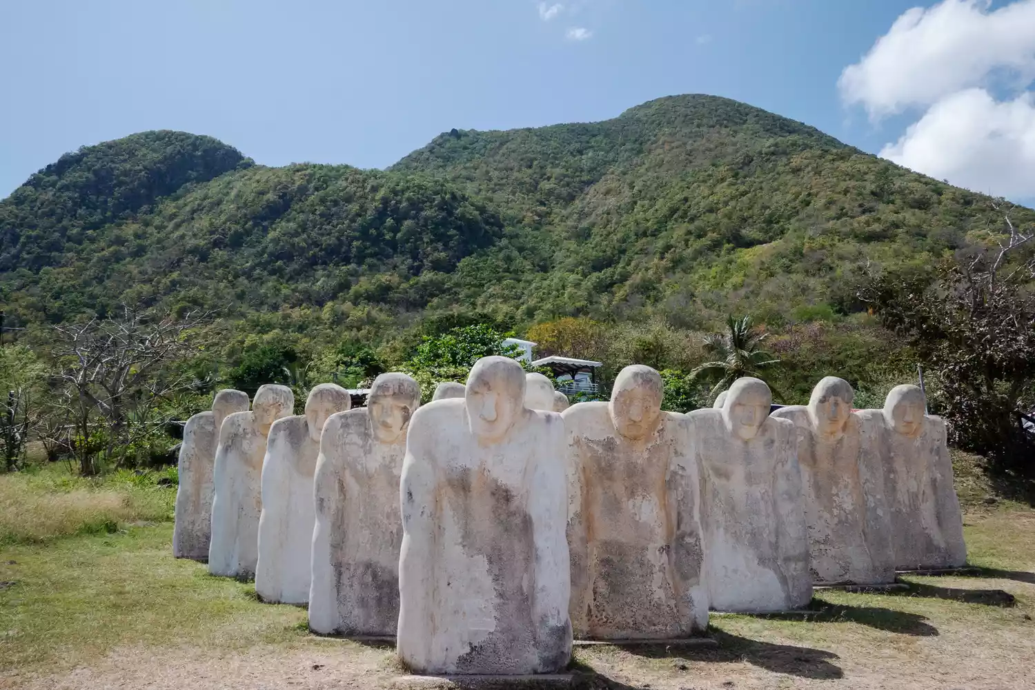 Large white stone statues of the Anse Cafard Slave Memorial facing the sea.