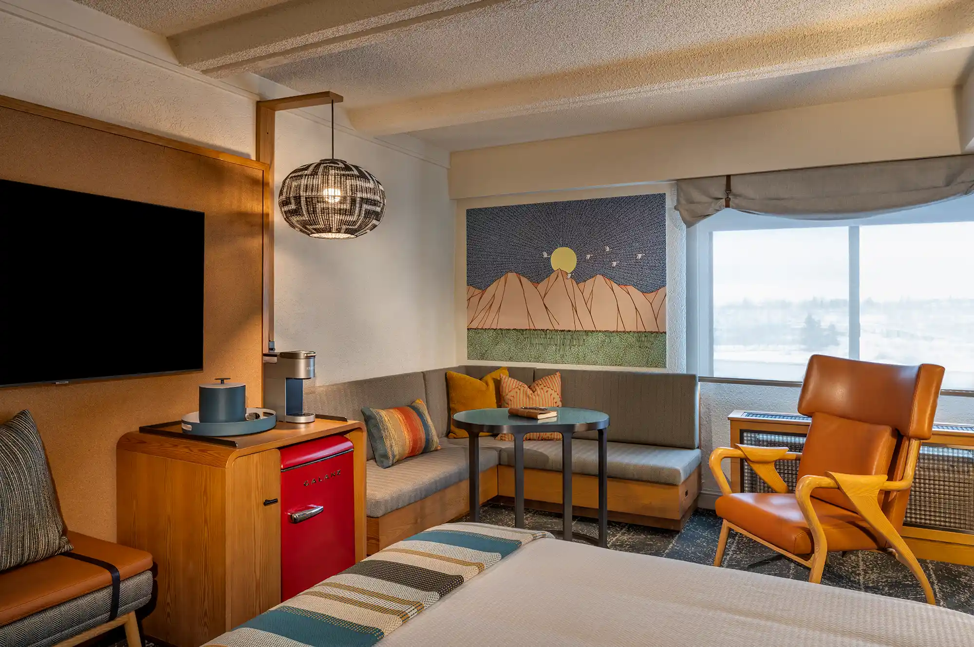 A cozy hotel room with a large window and a wall featuring mountain-inspired artwork.
