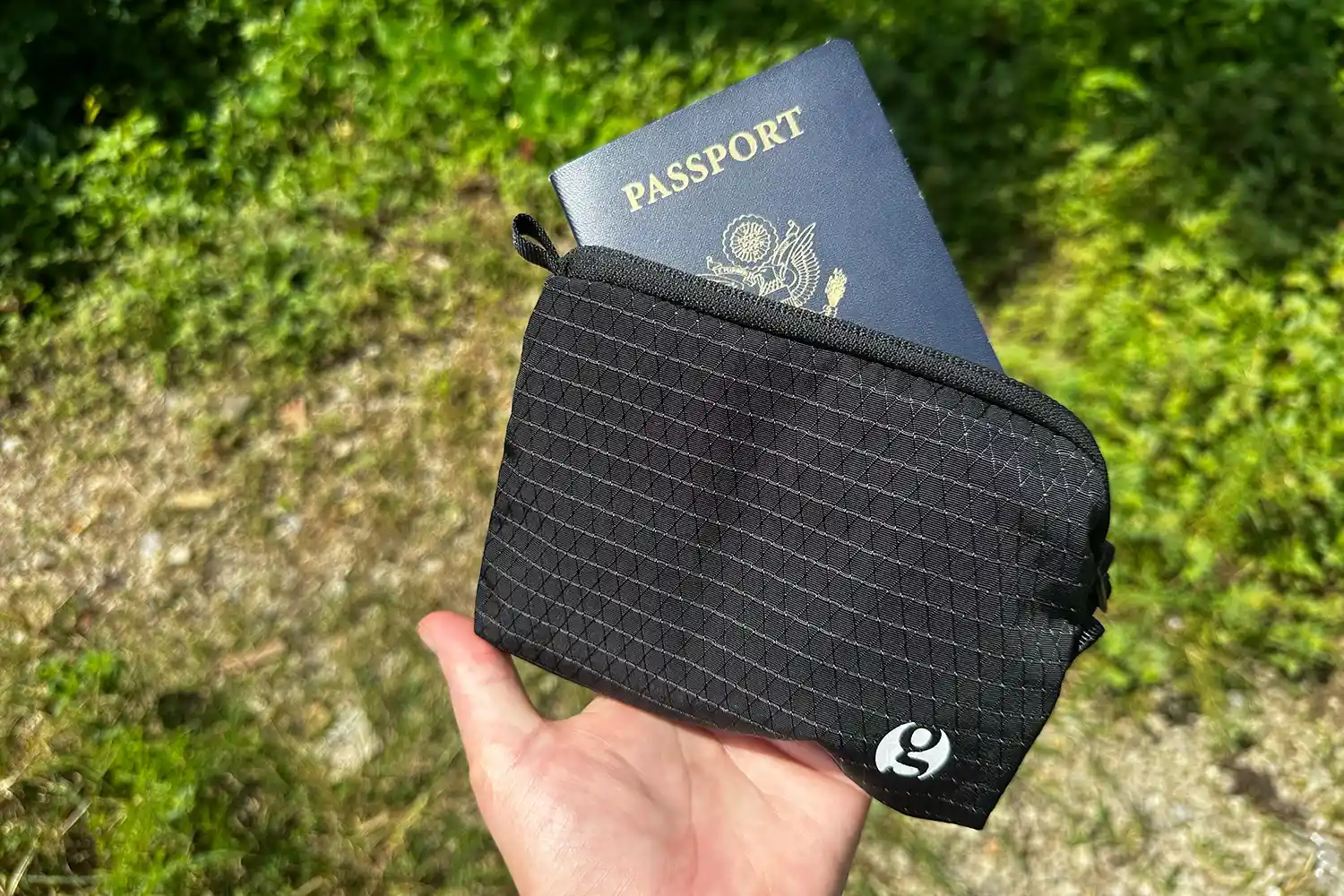 A person holding a black zippered travel pouch with a passport inside.