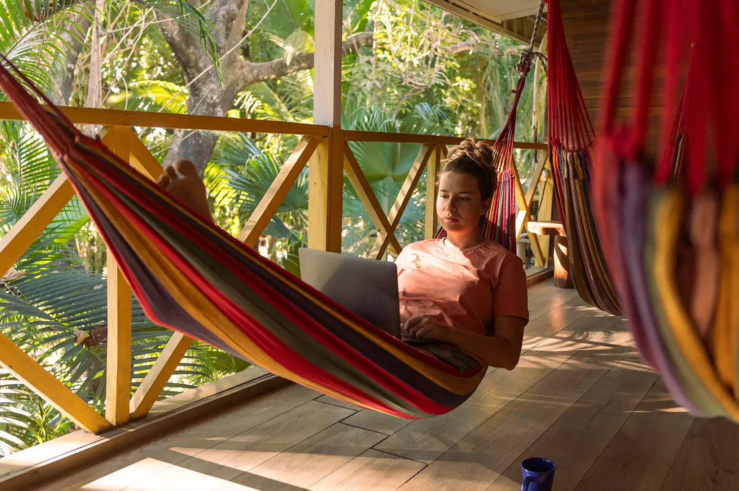 A remote worker using a laptop while relaxing in a hammock on a tropical porch in Costa Rica.
