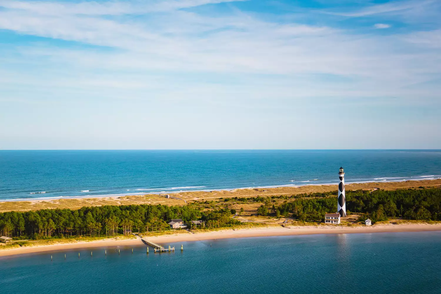 Aerial high-angle view of the Cape Lookout Lighthouse and the surrounding white sand beaches and blue ocean.