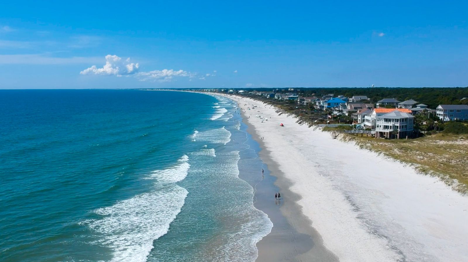 Aerial shot of a wide beach with many people enjoying the water and sand.