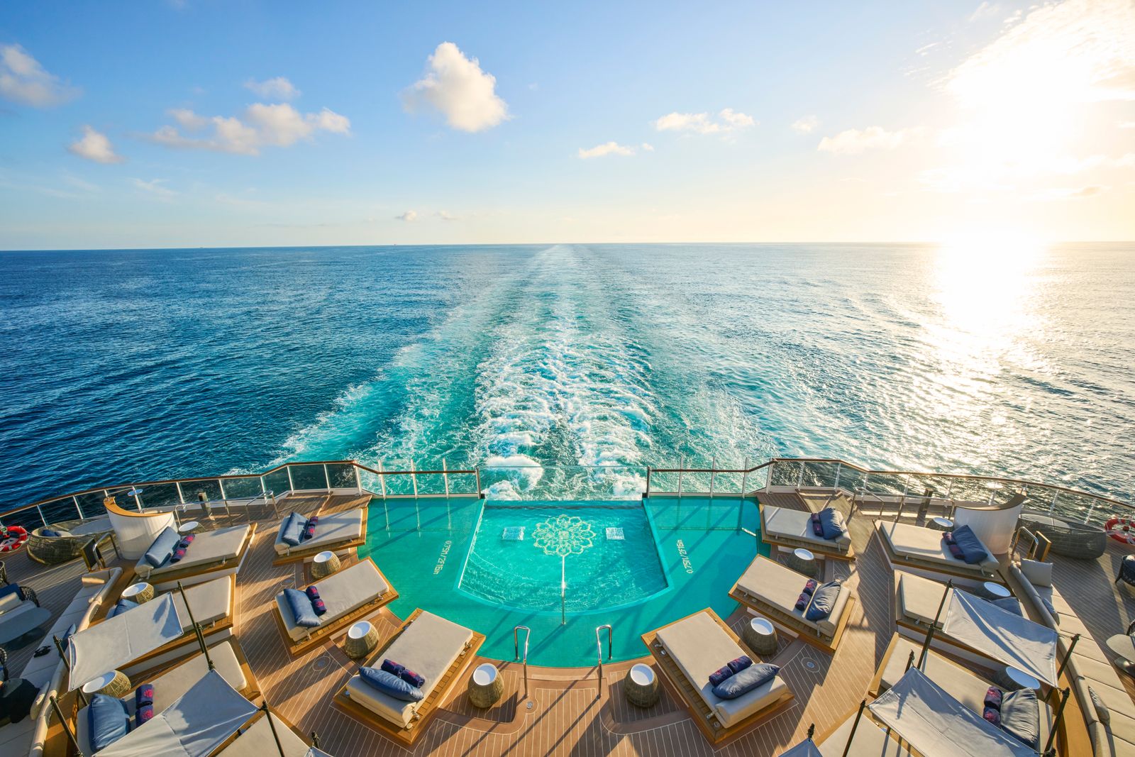 View of a luxury ship's upper deck featuring a swimming pool and sun loungers overlooking the sea.