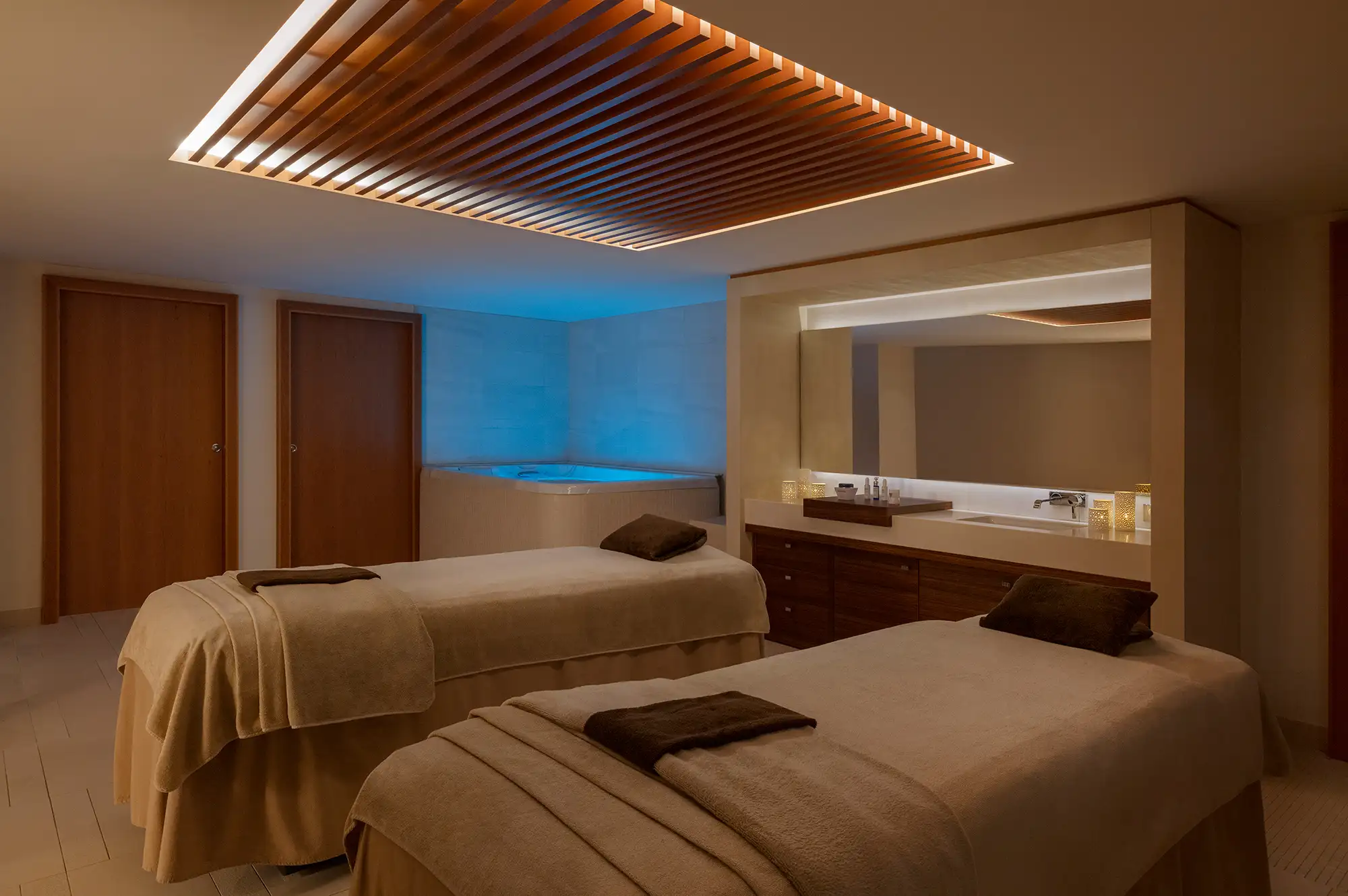 A serene spa treatment room with two massage beds and warm, ambient lighting.