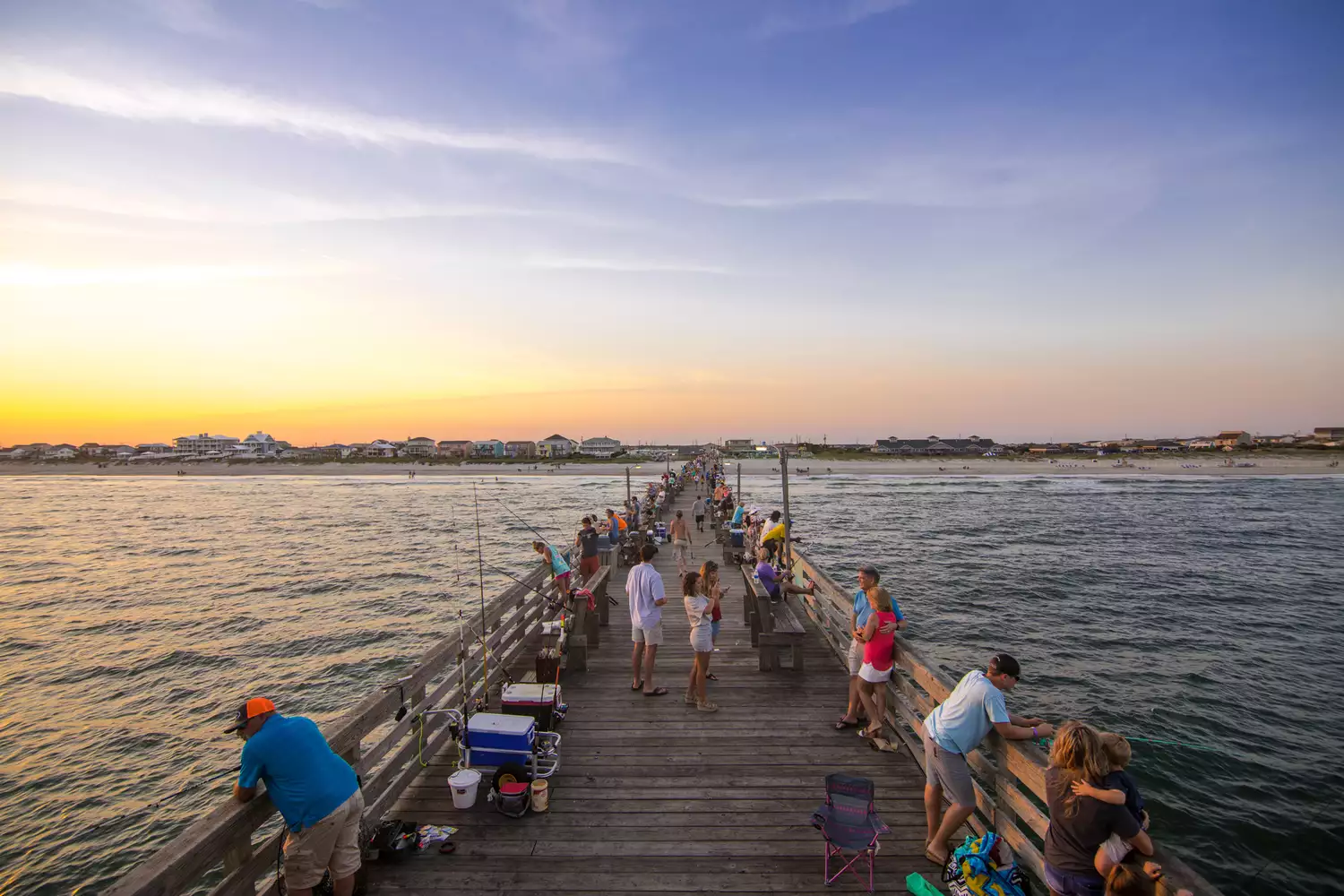 View from a bar overlooking the long Oceanana Fishing Pier at sunset with people fishing.