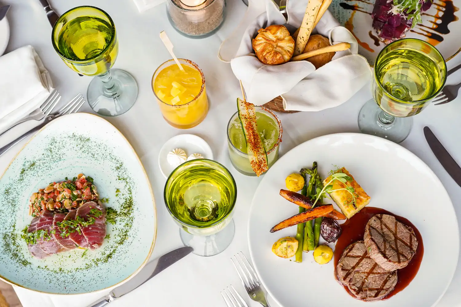 Exquisitely plated gourmet seafood and steak meals on a restaurant table.