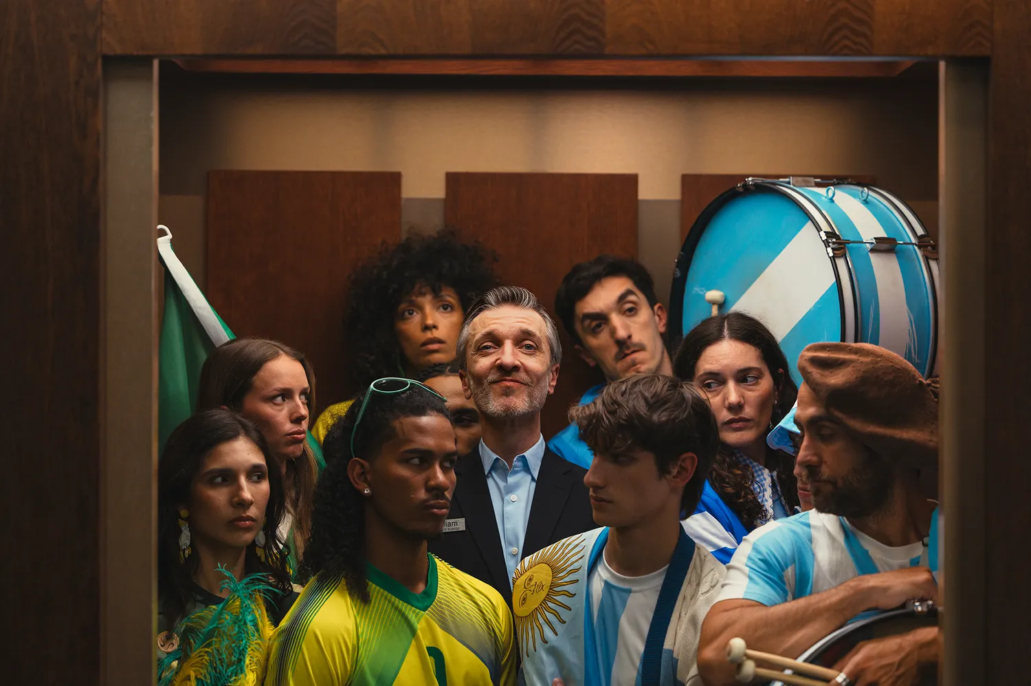 Global football fans in a hotel elevator wearing Brazilian and Argentinian jerseys.