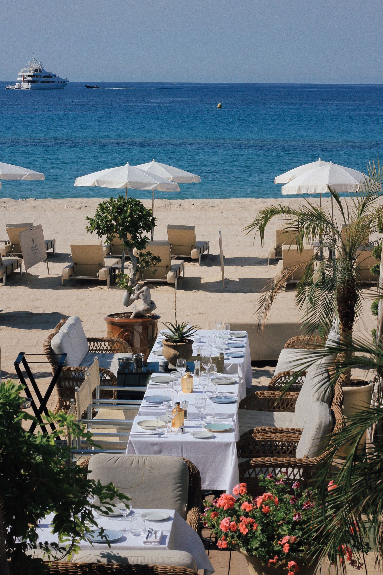 An outdoor luxury dining table set against a backdrop of the Mediterranean sea and a distant yacht.