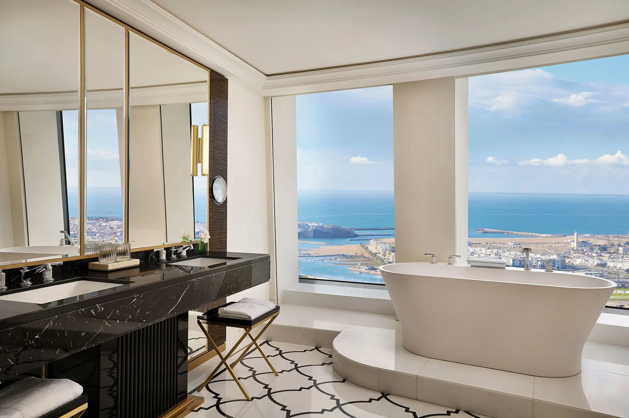 Luxury bathroom with a freestanding white bathtub positioned next to a large window overlooking the ocean.