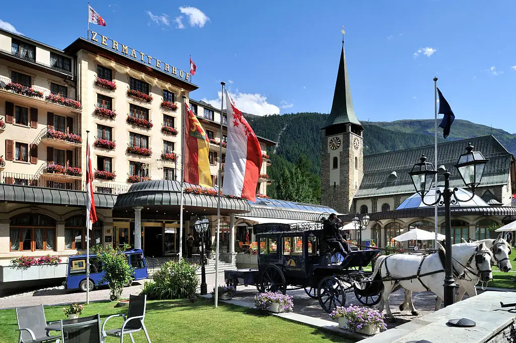 A horse-drawn carriage in front of a luxury hotel in Zermatt with the Matterhorn visible in the background.