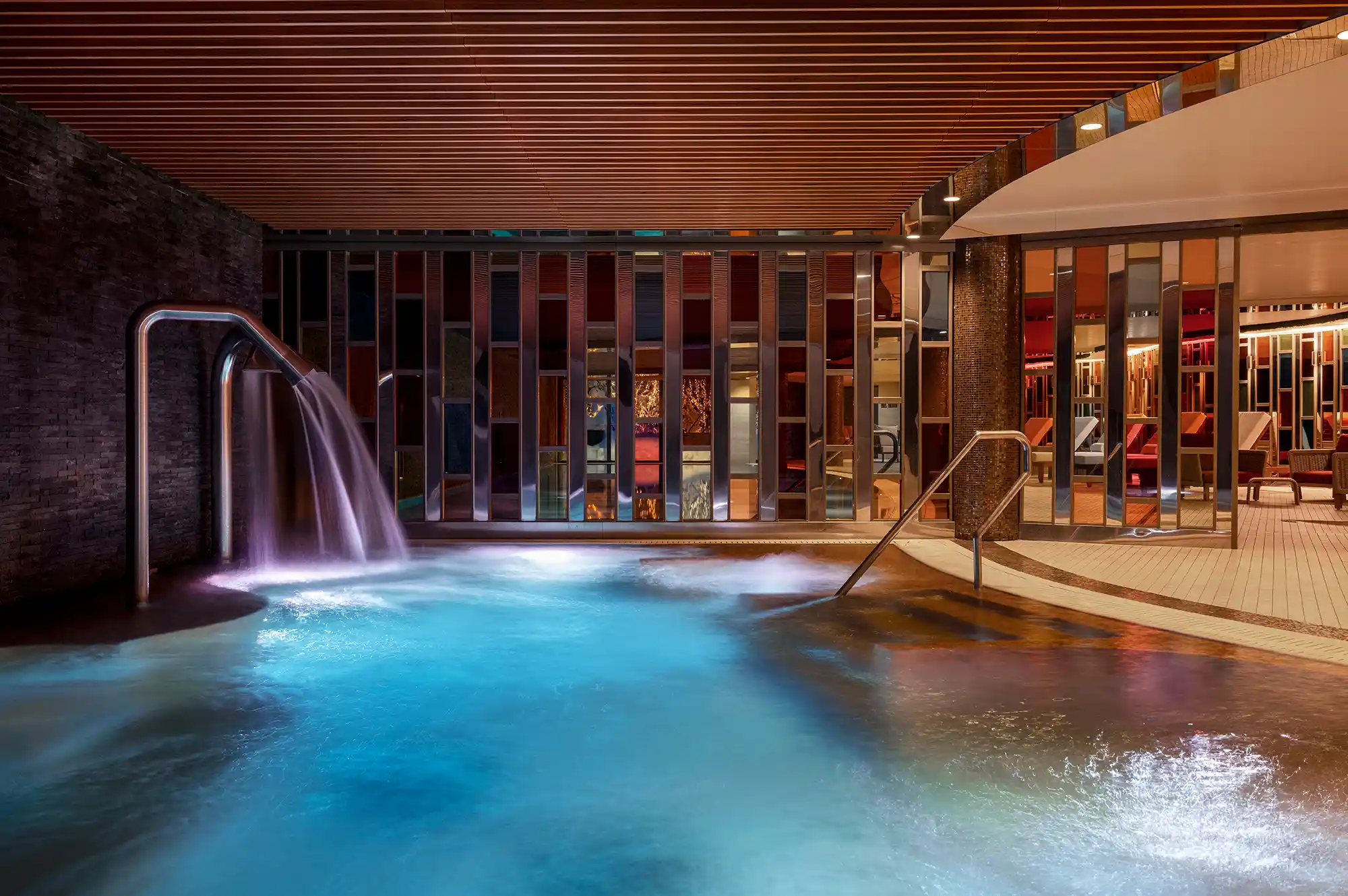 Large indoor swimming pool with stone walls and a modern waterfall feature.