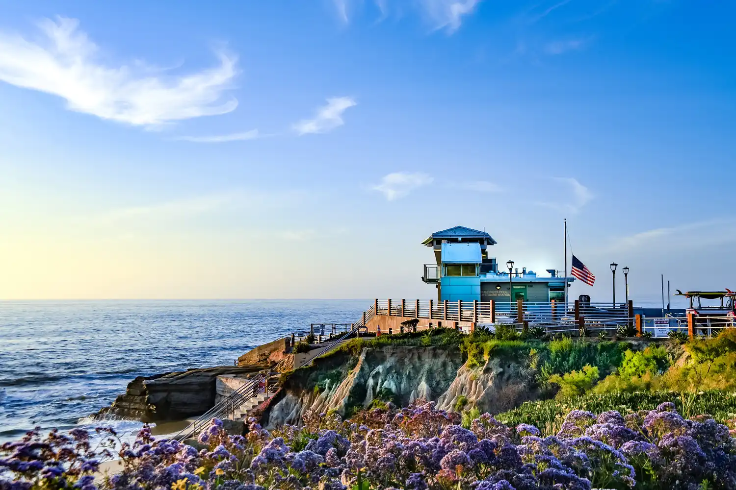 A coastal observation building on a rocky cliff in La Jolla California surrounded by blooming flowers.