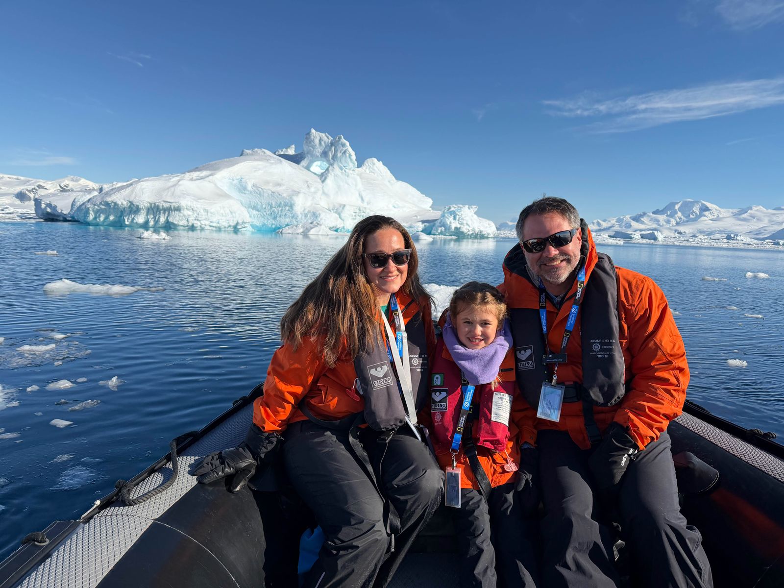 A close-up portrait of a traveler wearing a bright orange safety lifejacket and a hooded polar jacket.