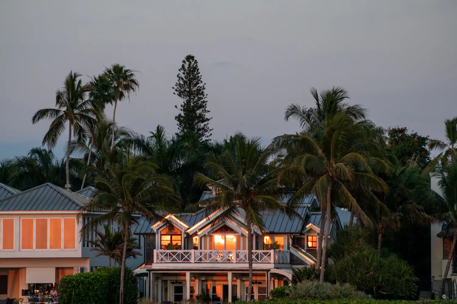 A luxury residential home in Naples Florida with palm trees and lit windows at dusk.