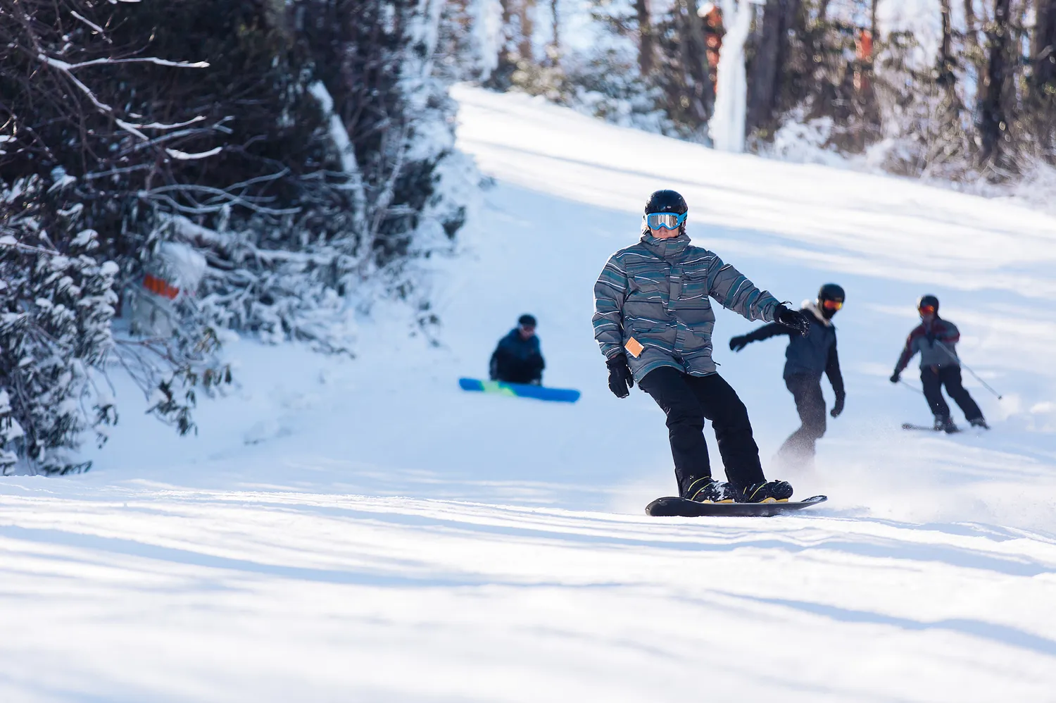 Snowboarder descending a snowy slope with other people skiing and snowboarding in the background.