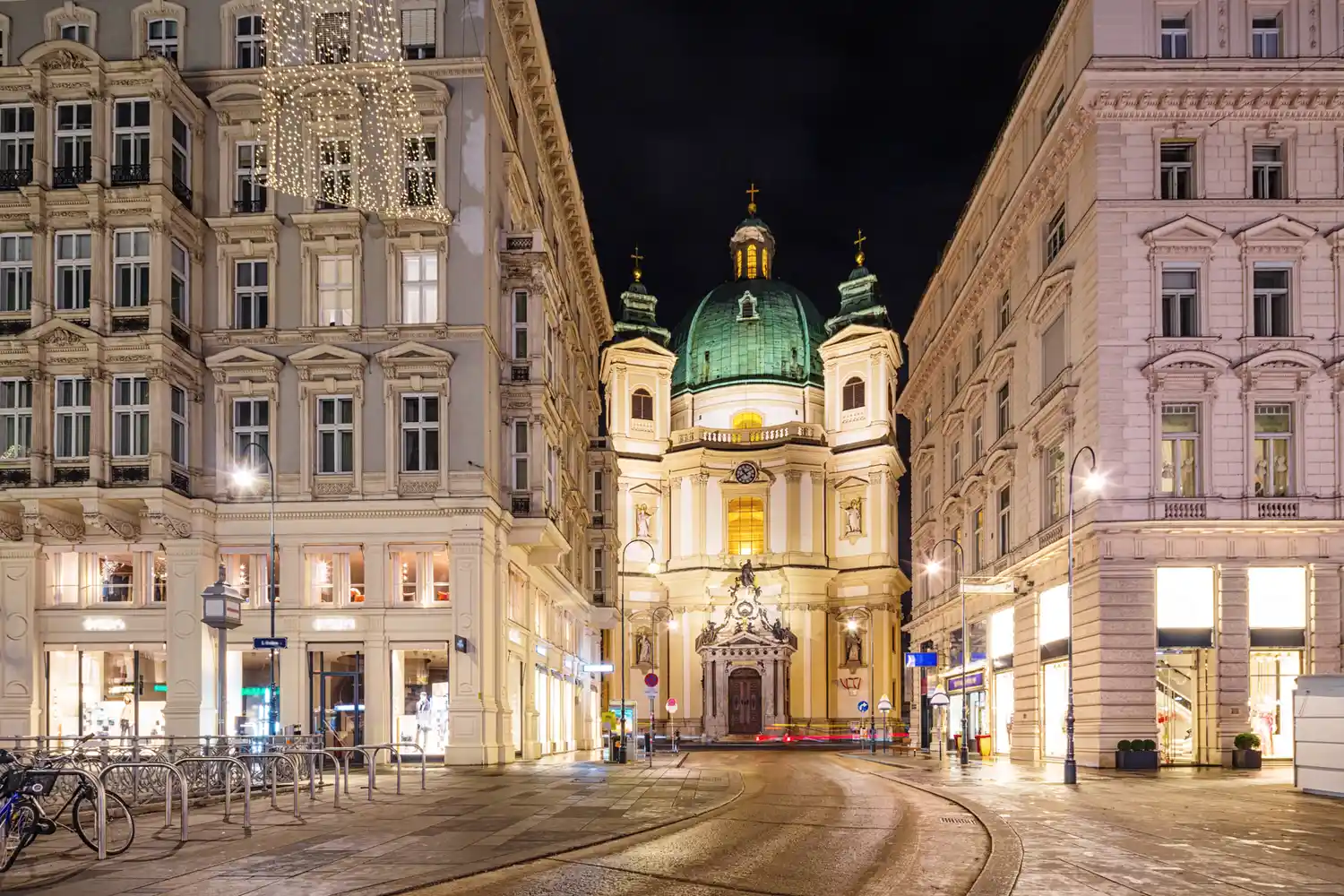 A baroque church at the end of a European city street lit at night in Vienna