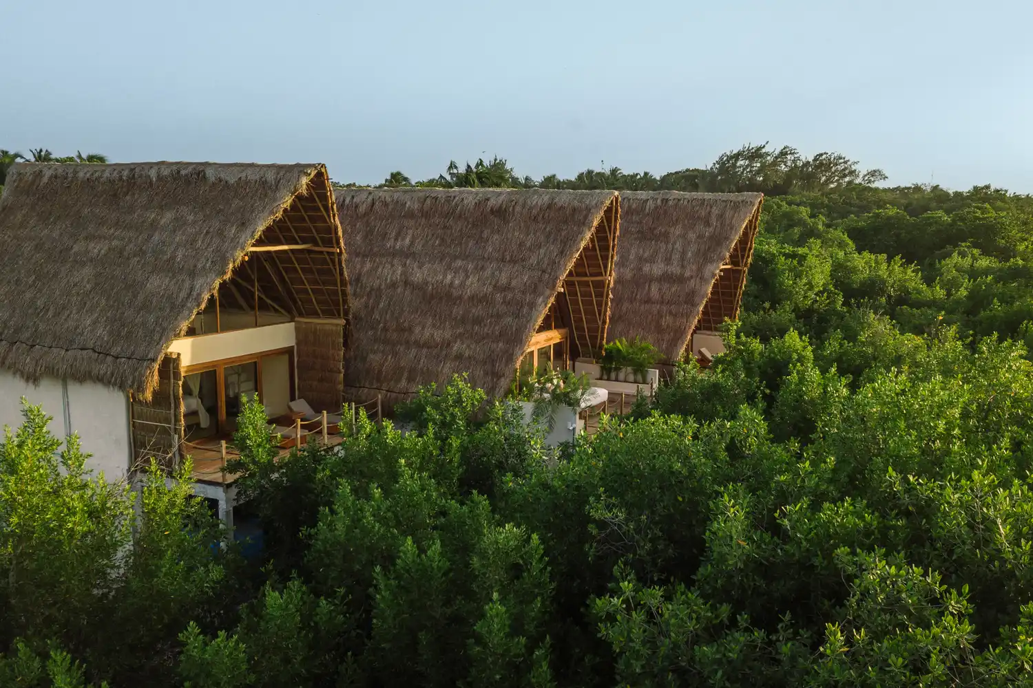 Thatched roof private villas at La Valise Tulum surrounded by dense jungle greenery.