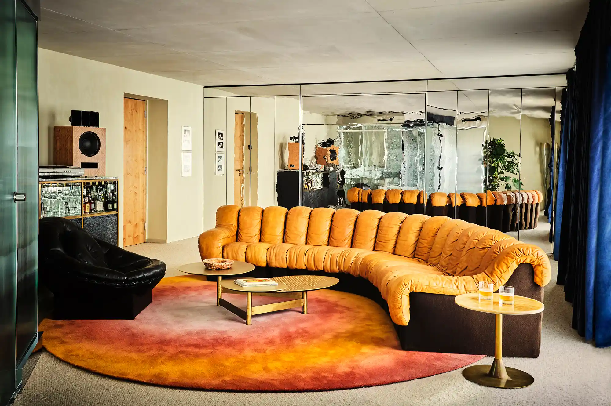 A modern lounge area with curved seating, colorful rugs, and glass walls.