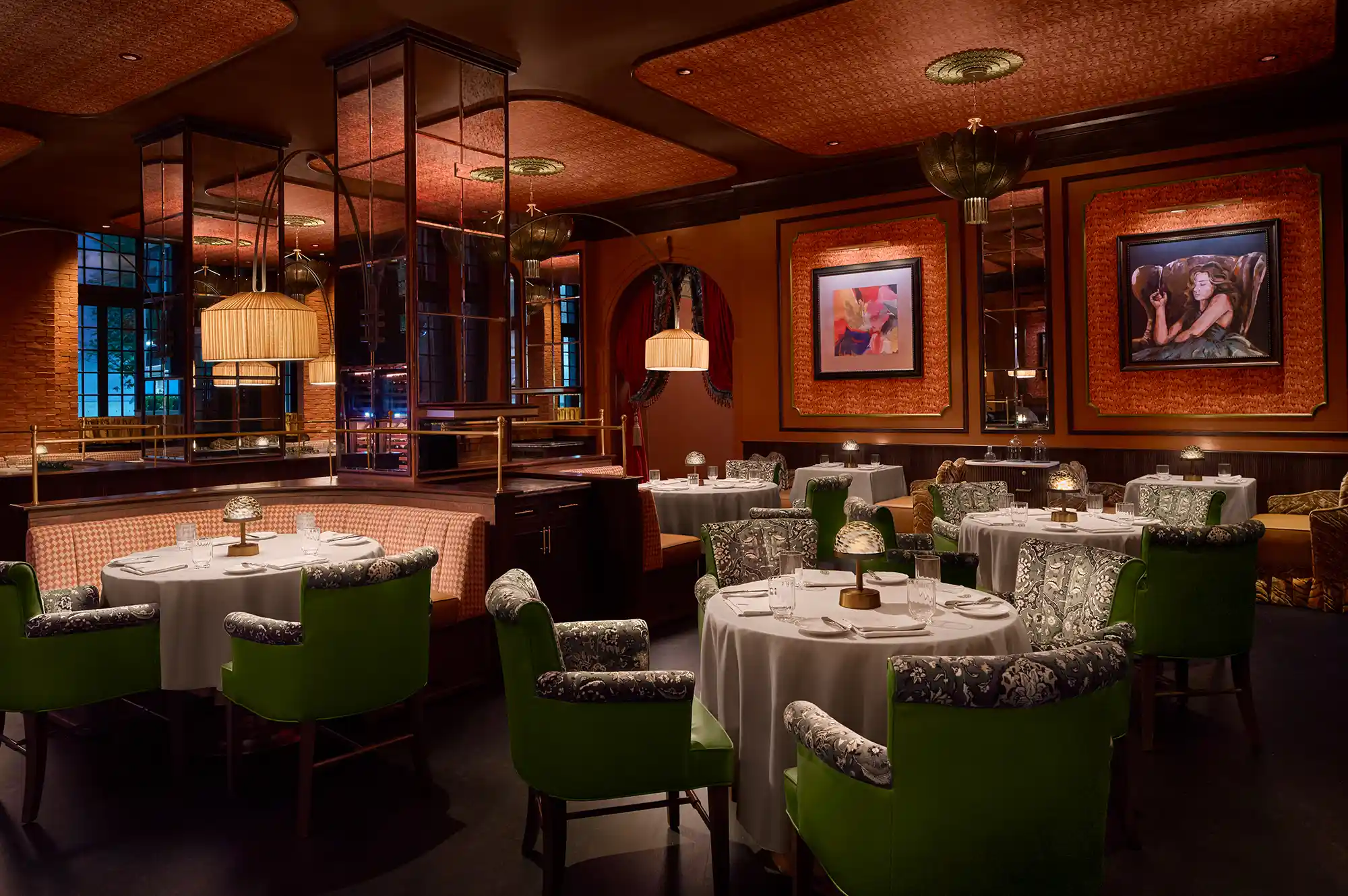 Upscale dining room with green velvet chairs, round tables, and gallery-style art on the walls.