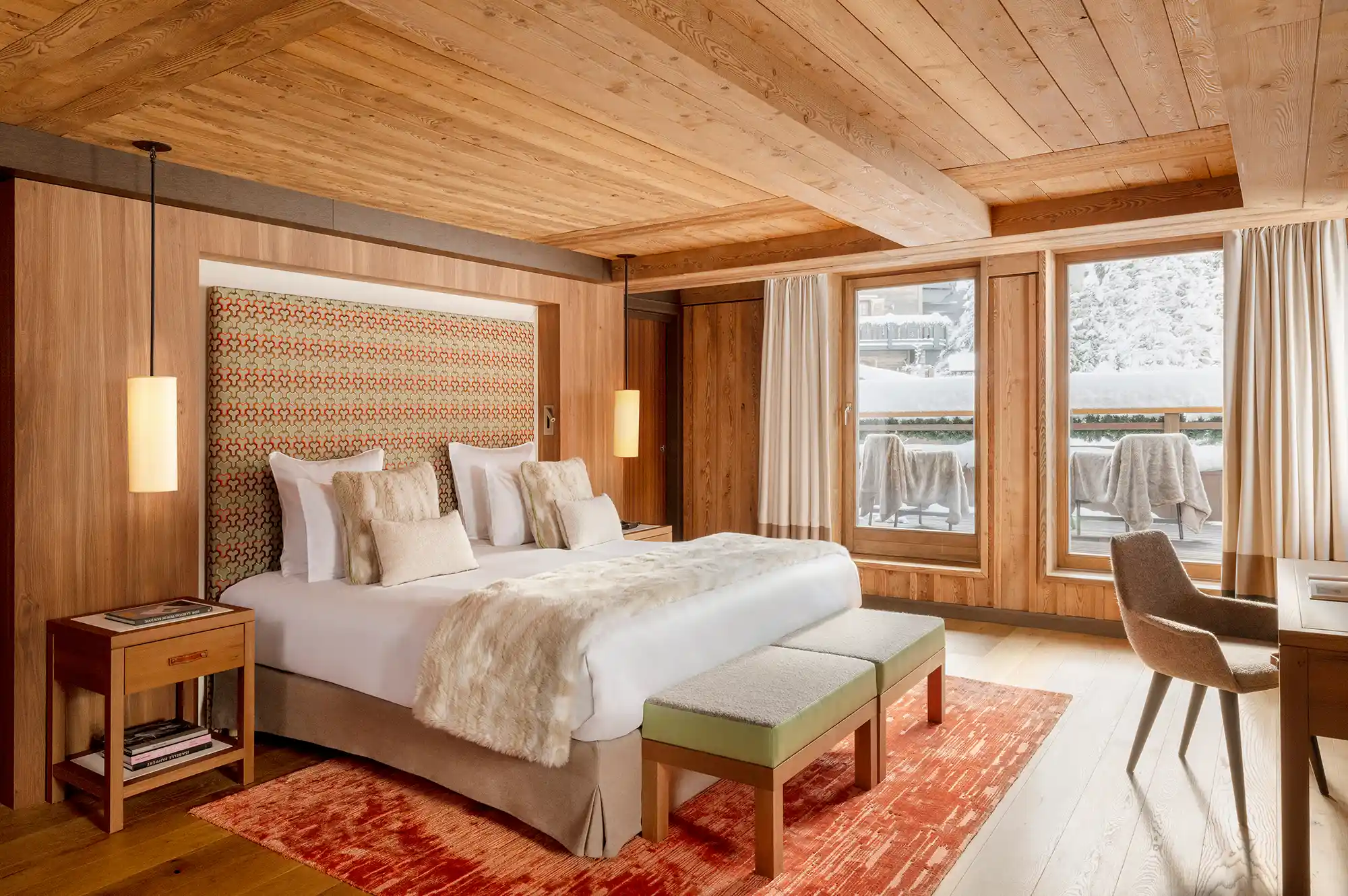 Luxury hotel room with wood paneling, a large bed, and views of the snowy mountains.