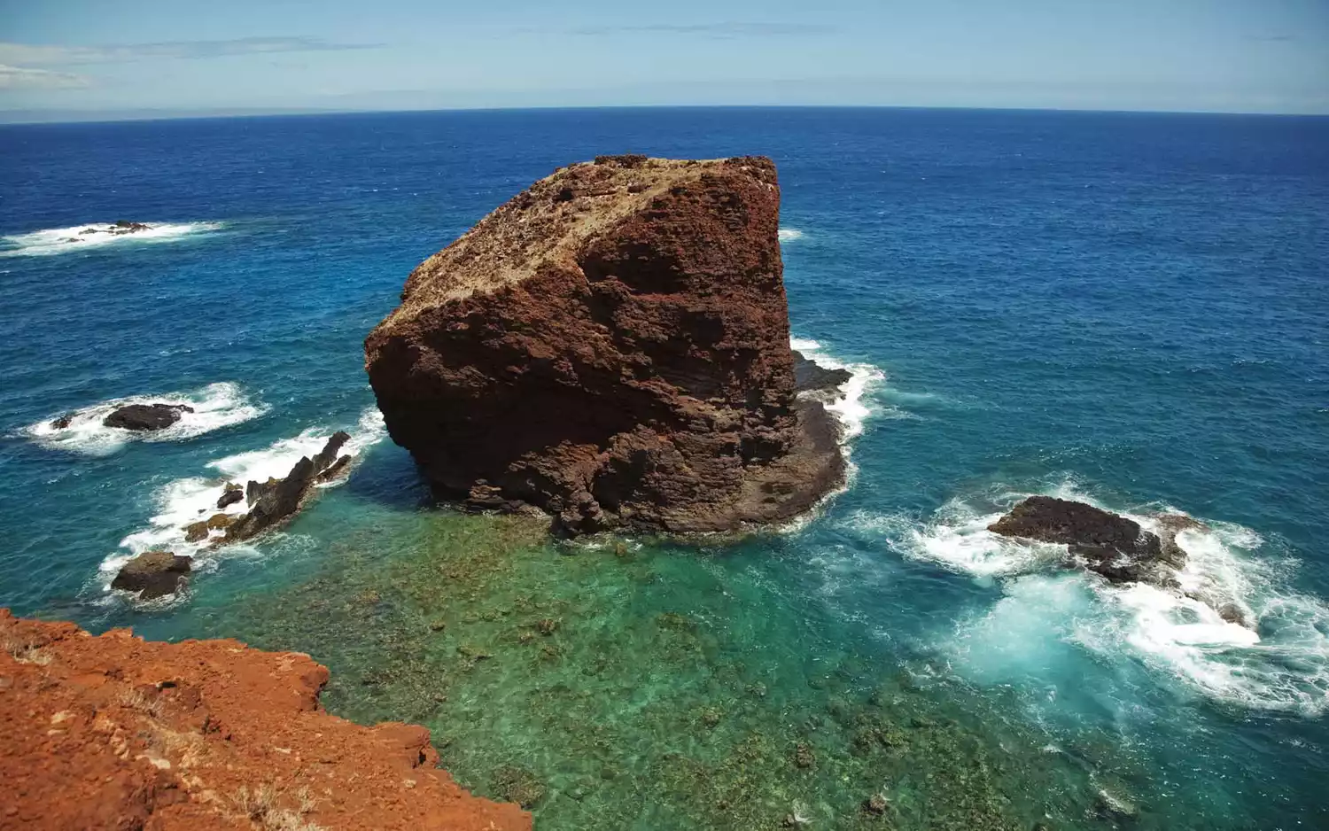 A massive rock formation known as Sweetheart Rock standing in the ocean waves off the coast of Lanai.