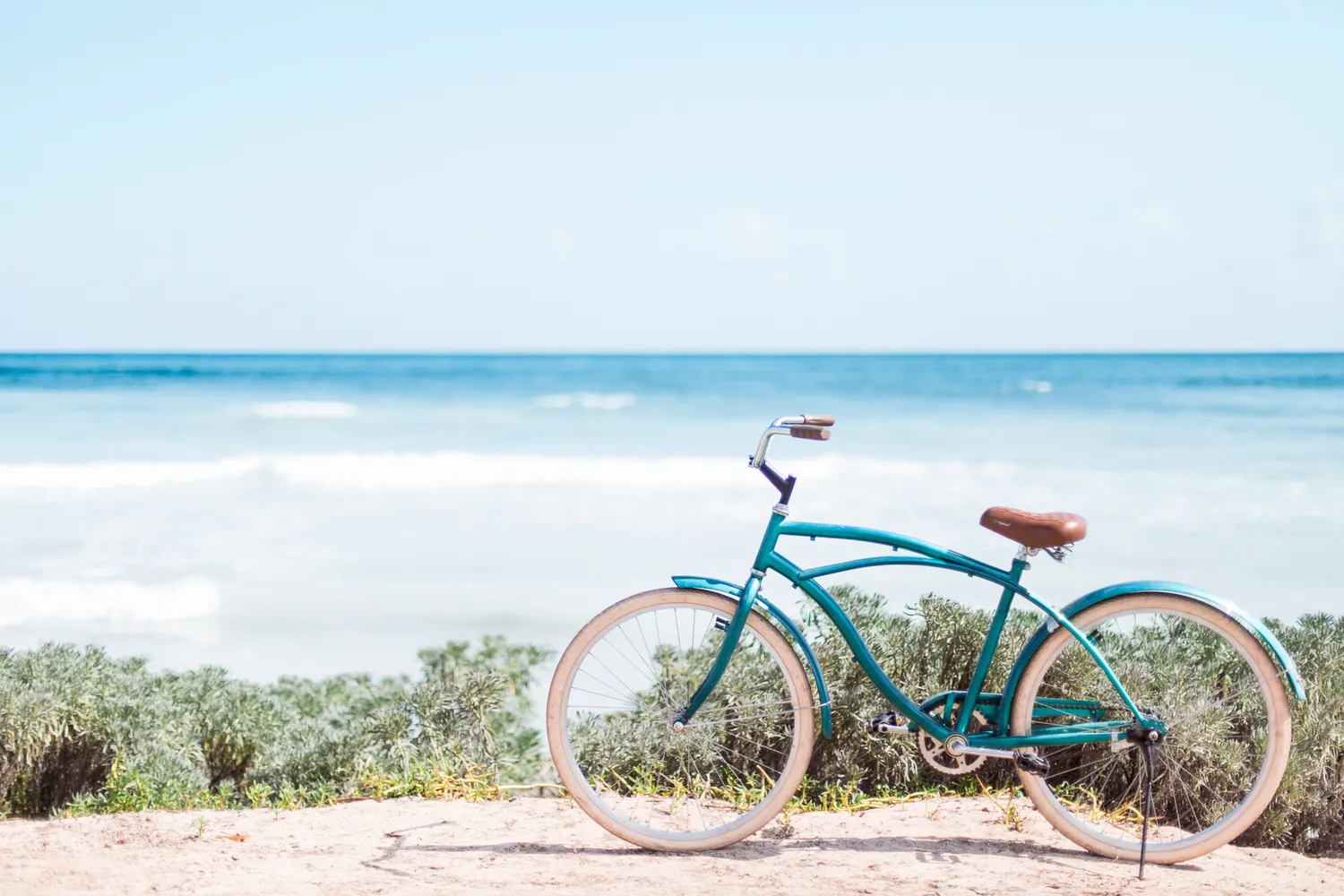 A bicycle parked on a sandy path near a Tulum beach with palm trees in the background.