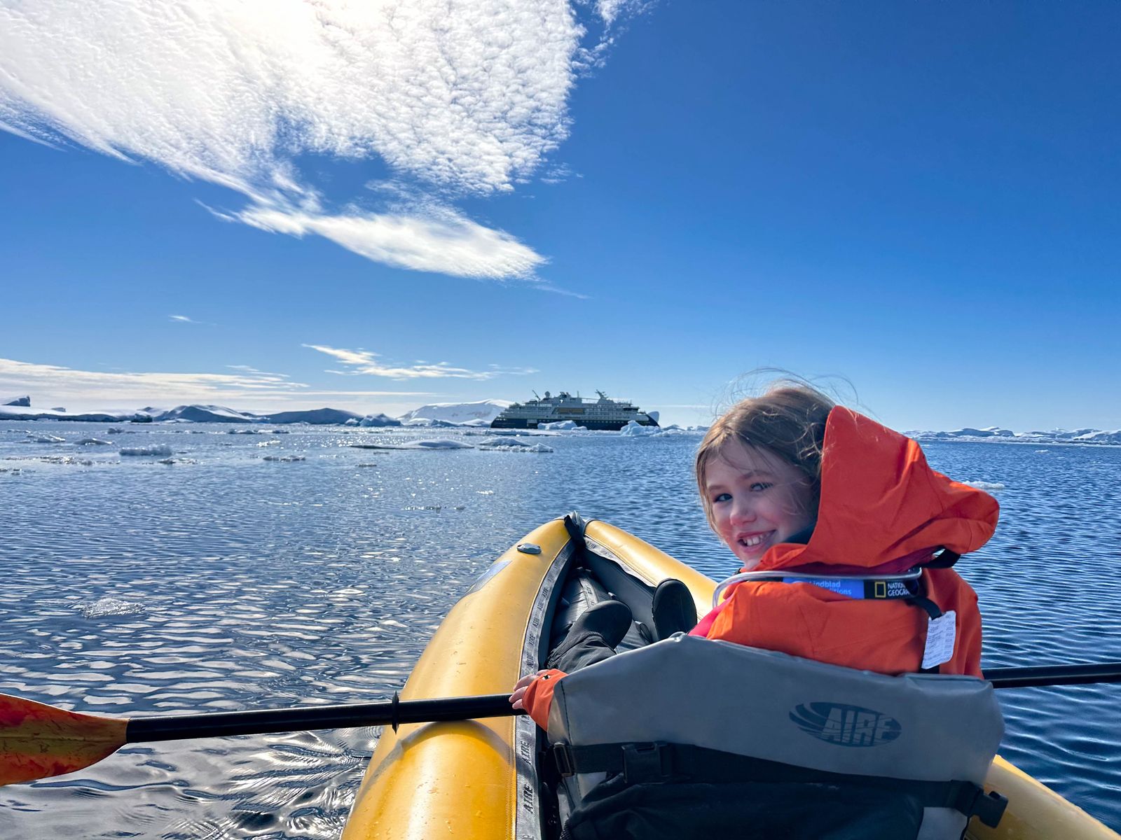 A group of travelers in a small boat or Zodiac exploring near the Antarctic coastline.