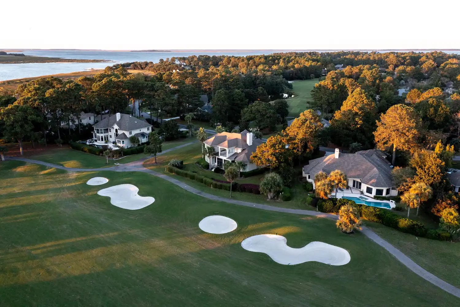 Aerial view of residential houses and a golf course nestled among trees near the Hilton Head coastline.
