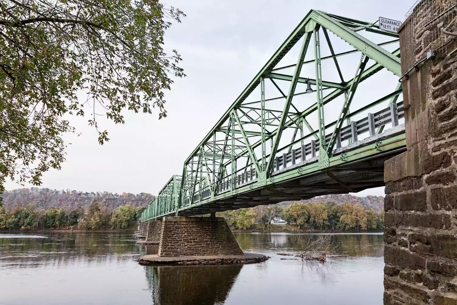 A wide shot of the truss-style Uhlerstown-Frenchtown Bridge crossing over the calm Delaware River.